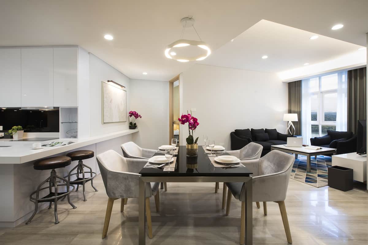 A modern kitchen with a central island, dining area with chairs and a table set for four, and a living area with a sofa and a coffee table.