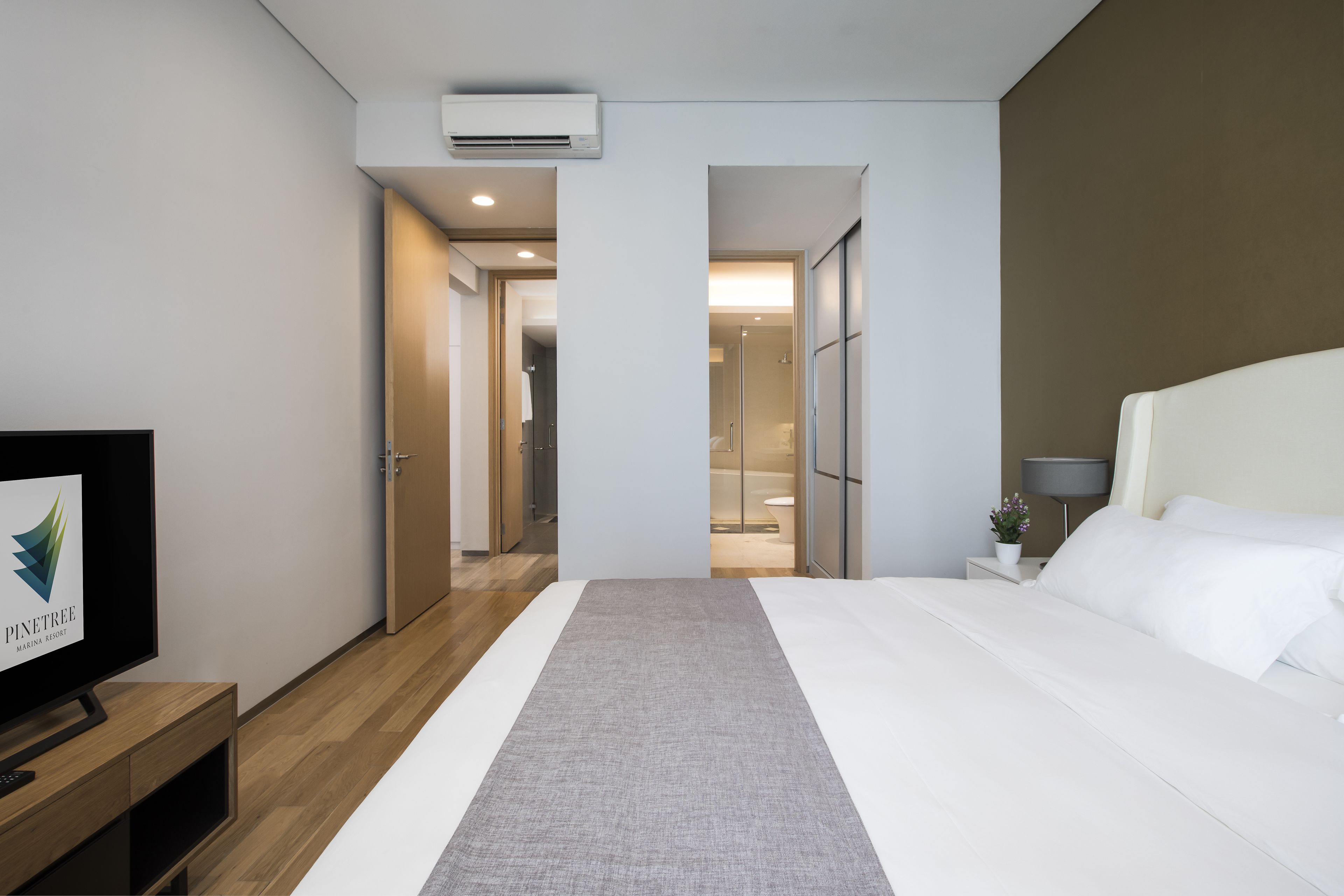 Una habitación de hotel con cama, televisión, mesita de noche y aire acondicionado.