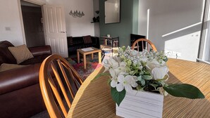 A living room with a brown leather sofa, a wooden dining table with chairs, a bookshelf, and a large window. - Seabreeze Apartment – Stunning Sea Views & Perfect Location (Eastbourne)