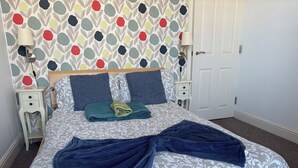 A neatly made bed with a patterned bedspread, two pillows, and folded towels. - Seabreeze Apartment – Stunning Sea Views & Perfect Location (Eastbourne)