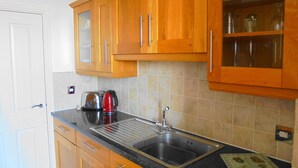 A kitchen with wooden cabinets, a stainless steel sink, and a kettle. - Seabreeze Apartment – Stunning Sea Views & Perfect Location (Eastbourne)