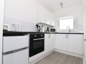 A modern kitchen with white cabinets, a black oven, a microwave, and a window above the sink.