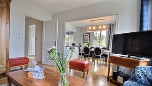 Ein Wohnzimmer mit Couchtisch aus Holz, einem roten Sofa, einem Fernseher auf einem Schrank und einem Essbereich mit Tisch und Stühlen.