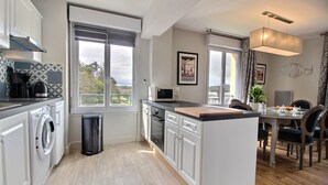 Eine moderne Küche mit einer zentralen Kochinsel, einem Essbereich mit Tisch und Stühlen sowie Blick durch die Fenster.