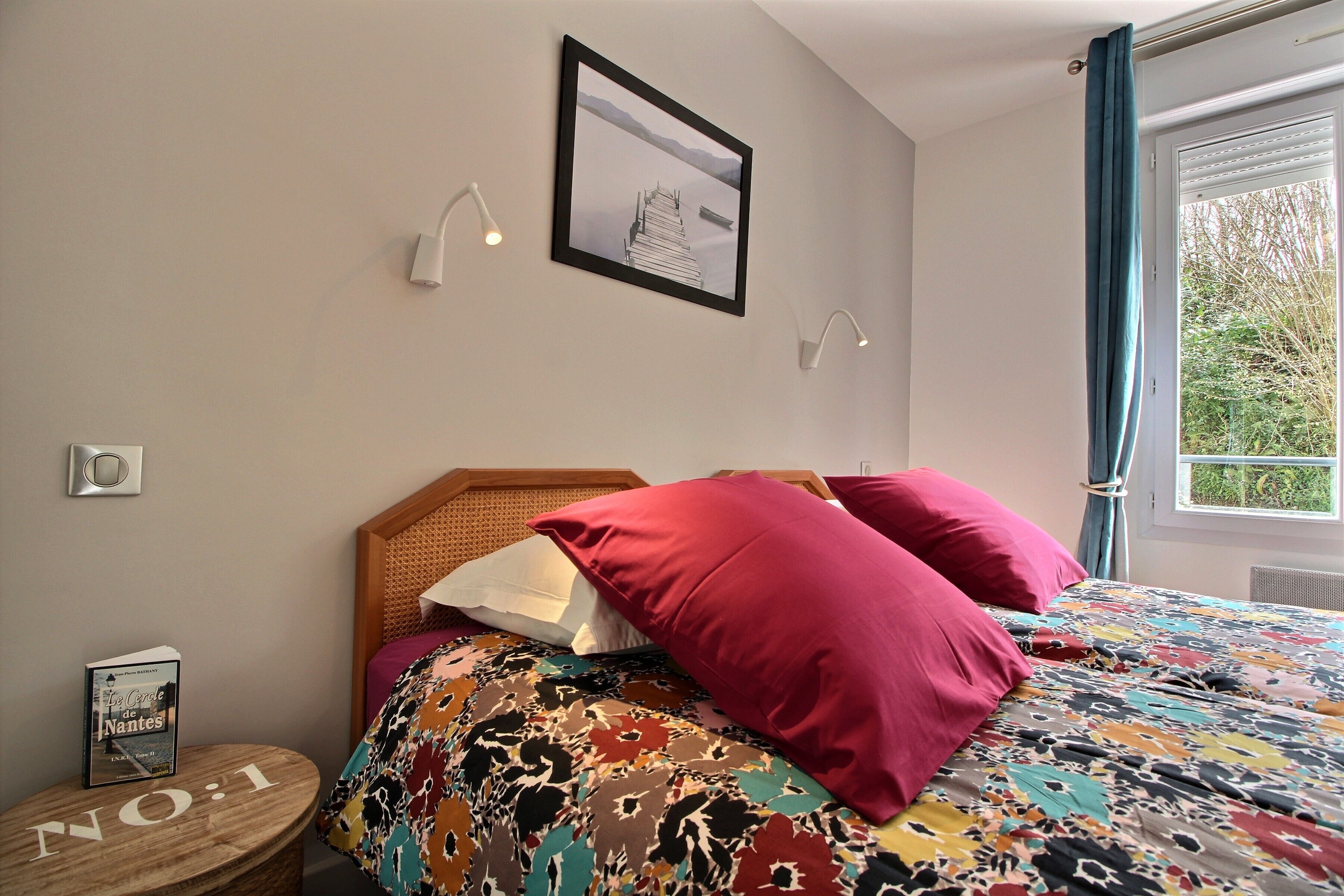 A bedroom with a bed, a framed picture on the wall, and a window with curtains.
