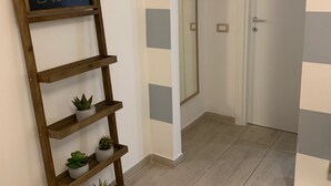 A hallway with a wooden ladder shelf holding potted plants, a chalkboard with text, a mirror, and striped wall panels.