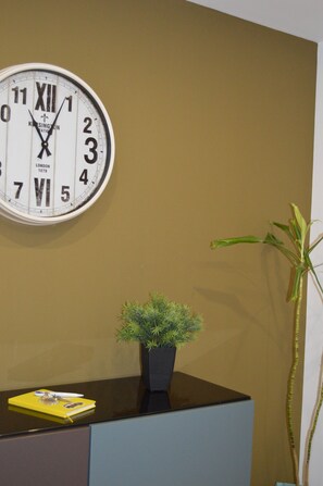 A wall clock with Roman numerals and a plant in a pot on a desk.