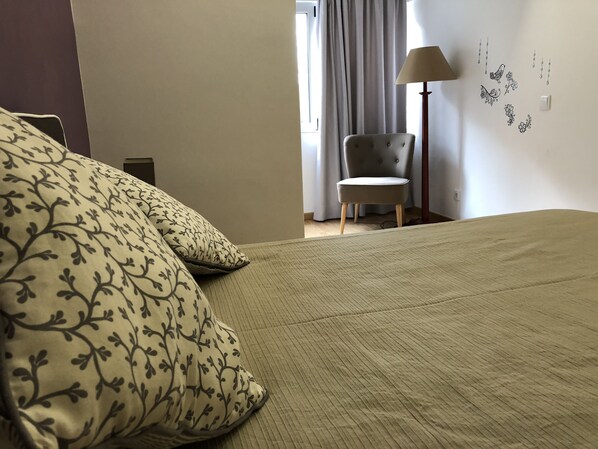 A bedroom with a bed, a chair, a lamp, and a window with curtains.