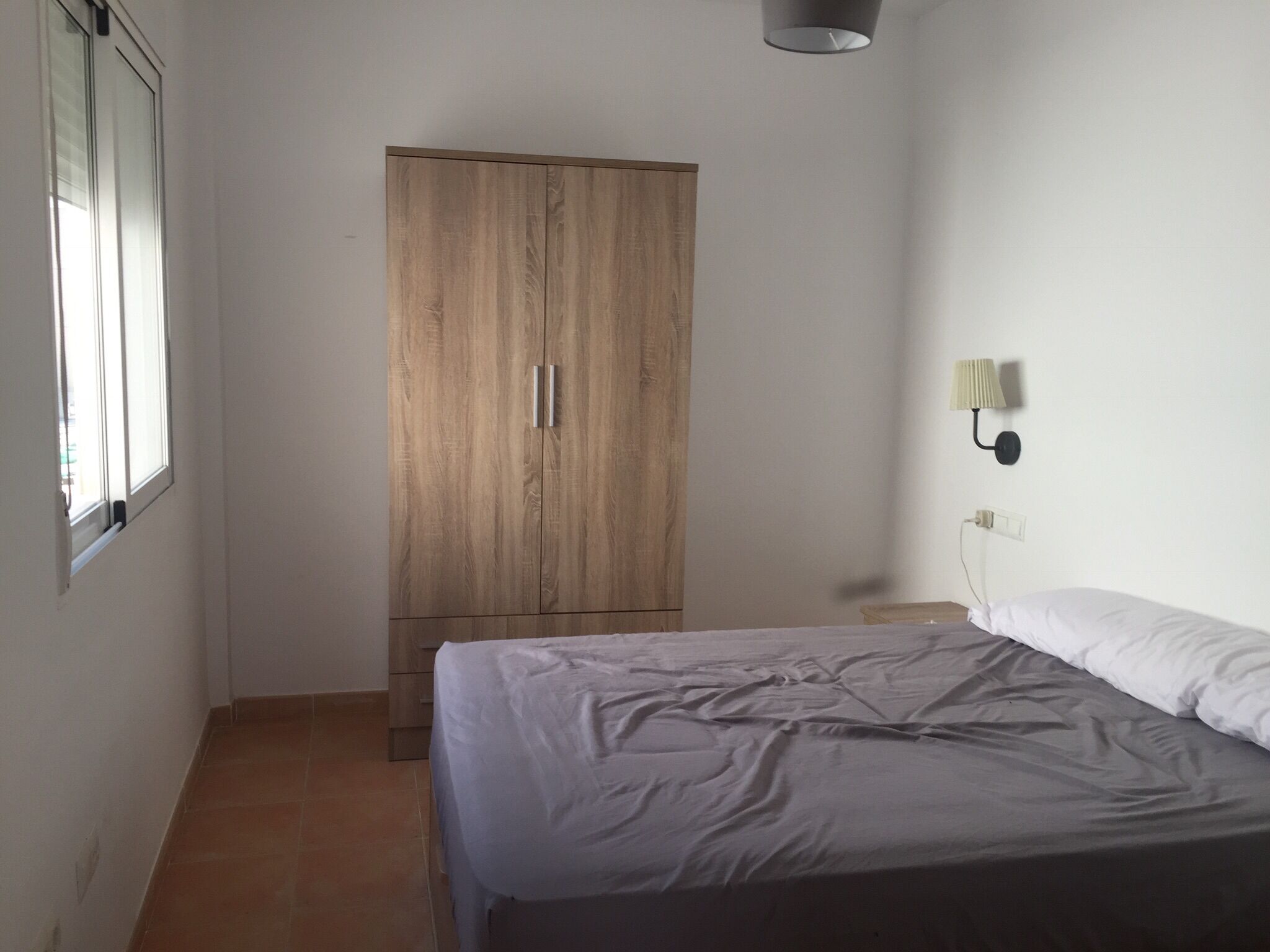 Een slaapkamer met een bed, een kledingkast, een raam en een wandlamp.