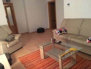 A living room with a glass coffee table, beige sofa, and a red rug.