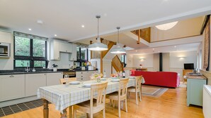 Une cuisine spacieuse équipée d’appareils électroménagers modernes, un coin repas avec une table et des chaises en bois, et un canapé rouge dans un salon lumineux doté d’un parquet et d’un escalier.
