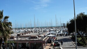 A marina with numerous boats docked, a pedestrian walkway, and a few buildings with signage. - Lori's Home near Rome. SPECIAL DISCOUNTS FOR YOU FOR AUTUMN AND WINTER. (Nettuno)