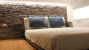 A bedroom with a stone-patterned headboard, a bed with a patterned bedspread, and a nightstand with a lamp. - Lori's Home near Rome. SPECIAL DISCOUNTS FOR YOU FOR AUTUMN AND WINTER. (Nettuno)