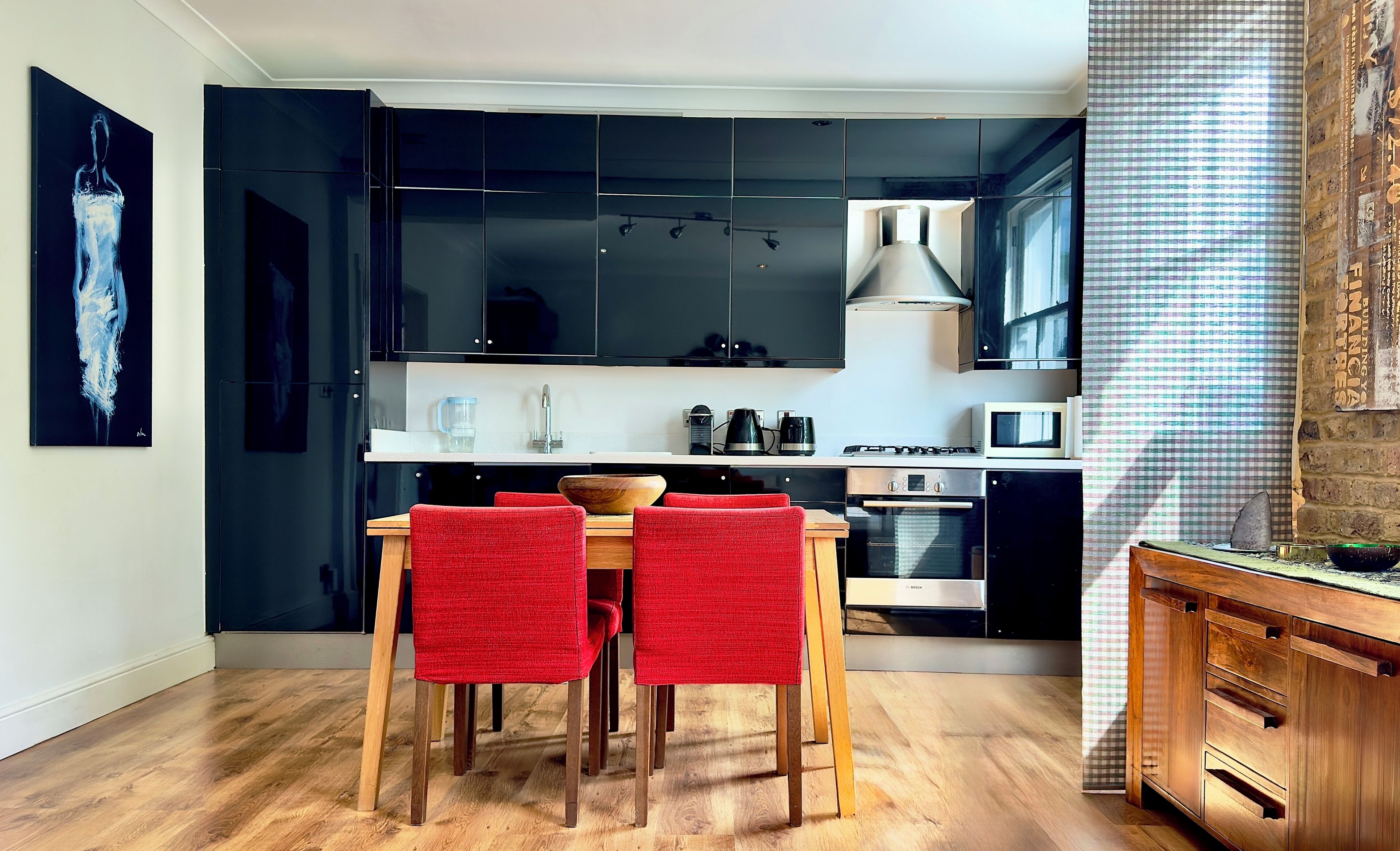 Una cocina moderna con armarios negros, encimera blanca y un comedor con sillas rojas.