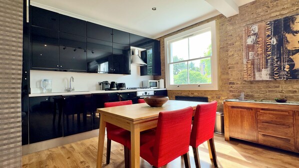 A modern kitchen with black cabinets, a wooden dining table, and red chairs. - * Stunning flat in South Kensington * (London)