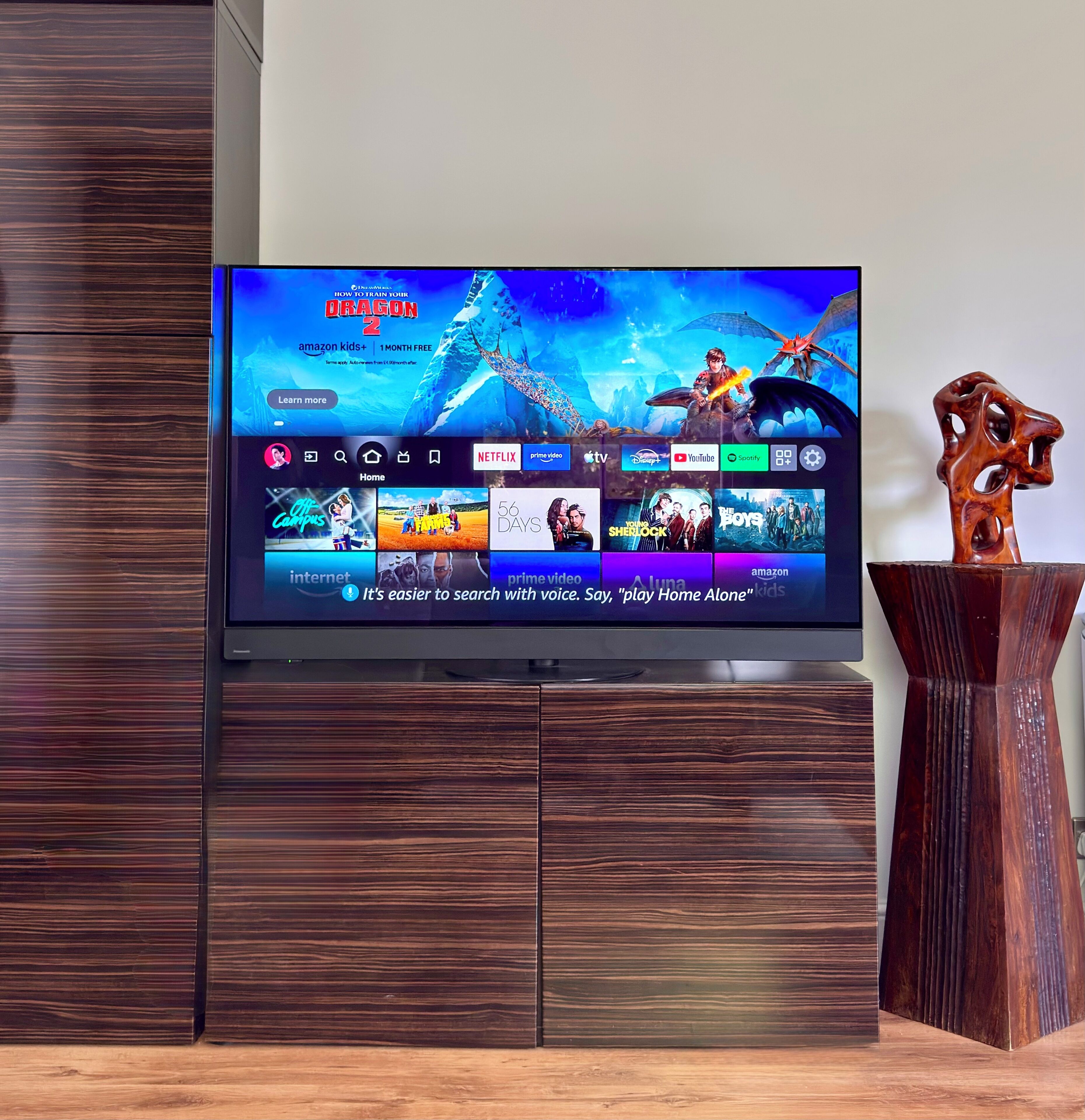 A flat-screen TV mounted on a wooden cabinet, displaying a streaming service interface with various content options.