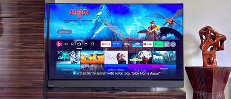 A flat-screen TV mounted on a wooden cabinet, displaying a streaming service interface with various content options.
