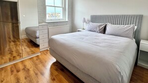 Quarto com cama grande, guarda-roupa, mesa de cabeceira com abajur e janela com vista para a cidade.