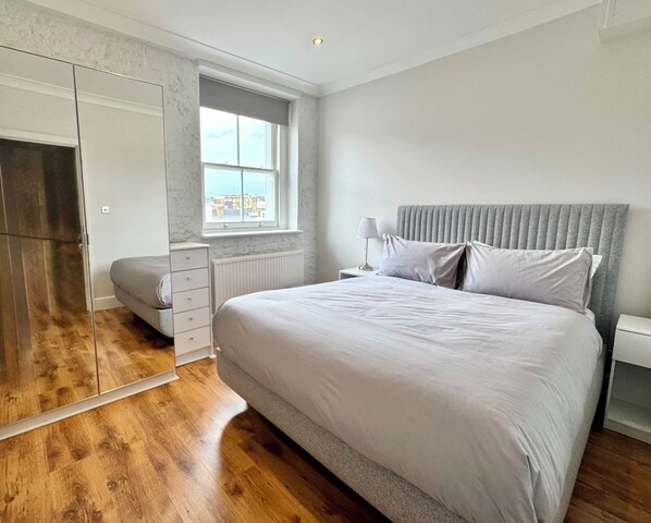 A bedroom with a large bed, a wardrobe, a bedside table with a lamp, and a window with a city view. - * Stunning flat in South Kensington * (London)