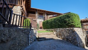 A stone staircase leading to a wooden balcony with a stone wall and a well-maintained hedge.