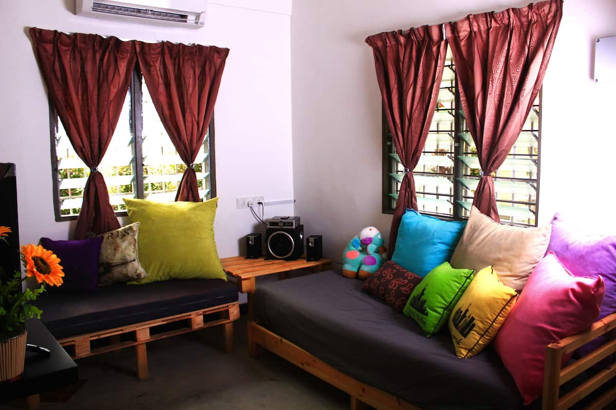 A cozy room with a wooden bench and a sofa, both with colorful cushions. There is a small table with a radio and a potted plant.
