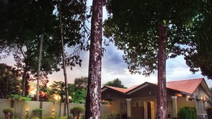 A house with a red roof, surrounded by trees and a well-lit garden. - The Retreat Homestay (Tanjung Malim)