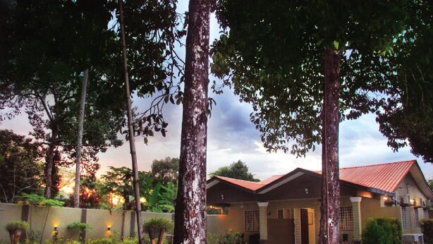 A two-story house with a red roof, surrounded by tall trees and a well-maintained garden. - The Retreat Homestay (Tanjung Malim)