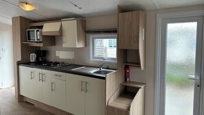 A modern kitchen with a microwave, stove, and sink. There is a window above the sink and a door with frosted glass. - Chalet Lynn on the beach and sea (Oosterschelde) (Kamperland)