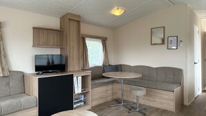 A modern, well-lit room with a flat-screen TV, a sofa, a small round table, and a bookshelf. - Chalet Lynn on the beach and sea (Oosterschelde) (Kamperland)