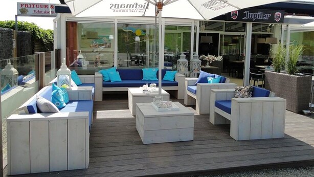 An outdoor seating area with white furniture and blue cushions, a large umbrella, and a sign for 'JUPILER'. - Chalet Lynn on the beach and sea (Oosterschelde) (Kamperland)