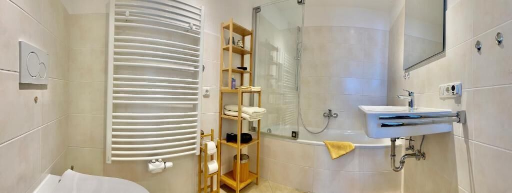 A modern bathroom with a bathtub, a glass shower enclosure, a wooden shelf with toiletries, and a white sink.