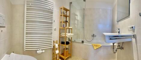 A modern bathroom with a bathtub, a glass shower enclosure, a wooden shelf with toiletries, and a white sink.