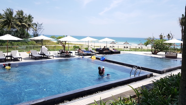 Ein Poolbereich mit Liegestühlen und Sonnenschirmen, ein kleiner Pool und Blick auf den Strand.