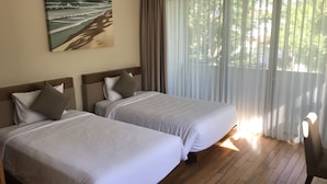 Ein Hotelzimmer mit zwei Betten, einem Bild an der Wand und Blick auf Grün hinter durchsichtigen Vorhängen.