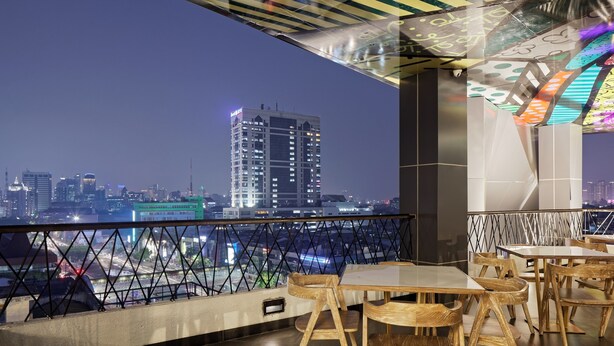 Un bar en la azotea con sillas y mesas de madera, vistas del horizonte urbano y una barandilla decorativa.