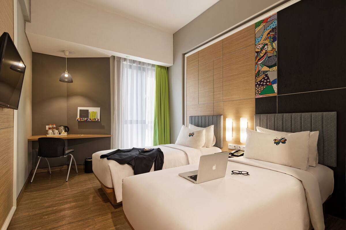 A hotel room with two beds, a desk with a chair, a TV, and a window with curtains.