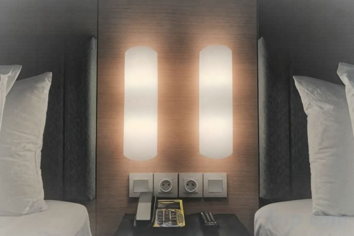 Habitación de hotel con dos camas, una mesita de noche con teléfono y controles remotos, e iluminación instalada en la pared.