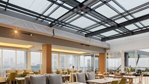 Un restaurante moderno con techos altos, amplios ventanales y una variedad de opciones de asientos, incluyendo cabinas y mesas.