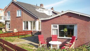 A two-story brick house with a patio area featuring red chairs and a small table.