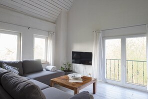 Ein modernes Wohnzimmer mit einem grauen Sofa, einem Holztisch und einem an der Wand montierten Fernseher.