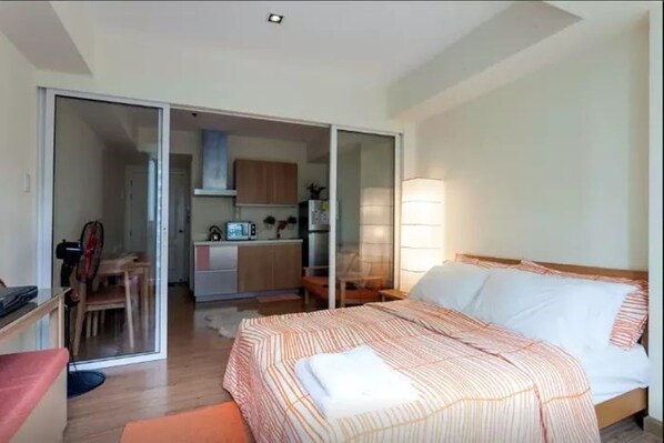 Une chambre à coucher comprenant un lit, un bureau et une porte coulissante donnant sur la cuisine.