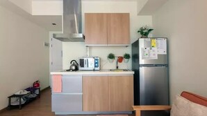 A compact kitchen with a built-in stove, a microwave, and a stainless steel refrigerator. - Santorini 1 Bedroom Condo at Azure Urban Residences (Parañaque)