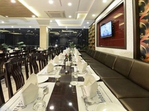 A restaurant with multiple tables set for dining, a television mounted on the wall, and a patterned wall decoration.