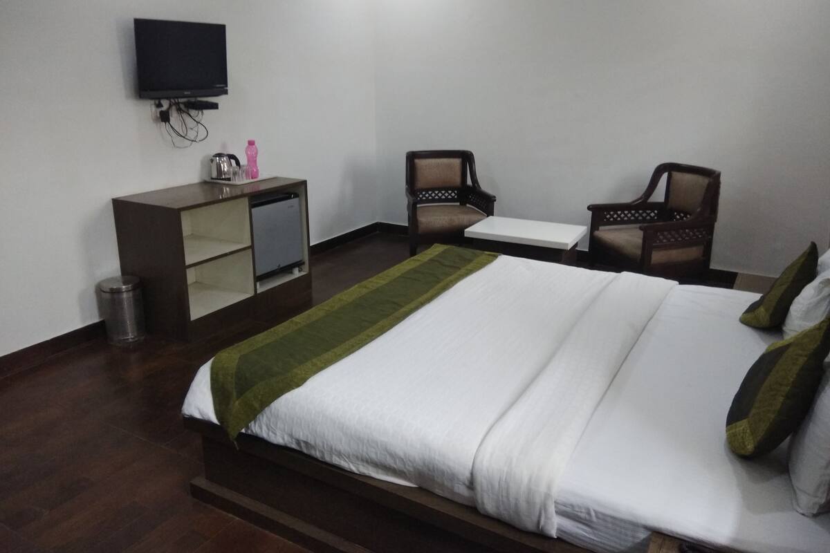 A hotel room with a bed, a TV mounted on the wall, a small desk, and two chairs.