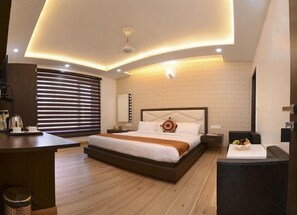A modern bedroom with a large bed, bedside tables, a desk, and a window with blinds.