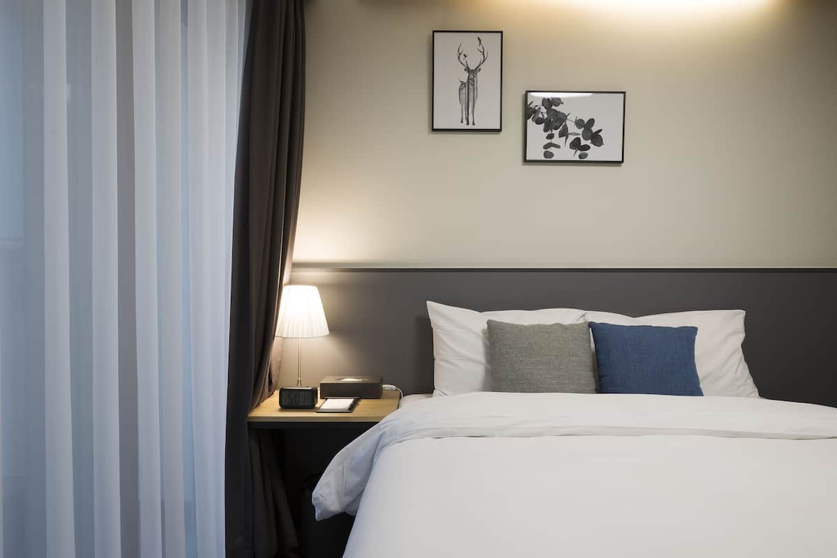 A hotel room with a bed, a nightstand, a lamp, and two framed pictures on the wall.