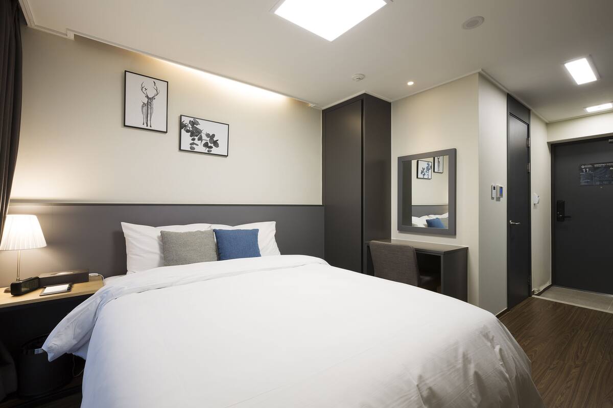 A hotel room with a bed, bedside table, lamp, artwork on the wall, and a mirror.