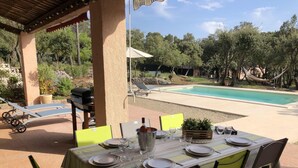 An outdoor dining area with a pool view, including a table set for four, chairs, and a grill.