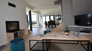 Een moderne woonkamer met een houten eettafel, een blauwe poef en een flatscreen-televisie.