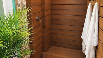 A wooden shower enclosure with a built-in showerhead, a towel rack, and a potted plant.